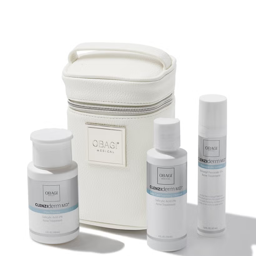 A collection of Obagi Clenziderm Acne Therapeutic System products displayed in front of a white case, including a foaming cleanser, therapeutic lotion, and a zippered case.